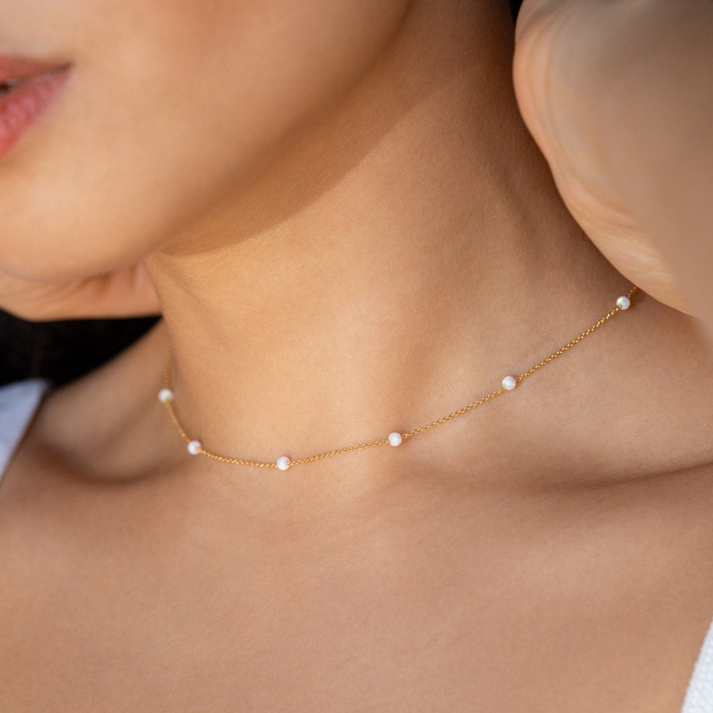The Opal Station Necklace is a delicate handmade piece featuring small pearls and opals, designed to rest close to the neck. This minimalist necklace beautifully complements light skin tones.