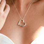 A woman wears a Custom Bead Heart Necklace with a silver heart pendant and small lock, paired with a strapless white top.