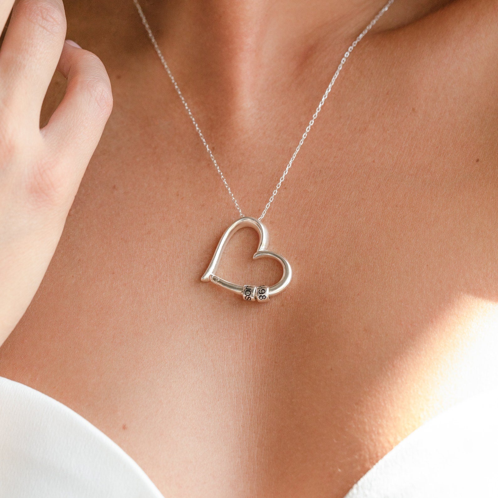 A woman wears a Custom Bead Heart Necklace with a silver heart pendant and small lock, paired with a strapless white top.