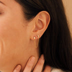 Close-up of a woman's ear wearing Luna Moon & Star Chain Earrings, featuring a delicate chain linking the moon and star studs and accenting her cartilage piercing.