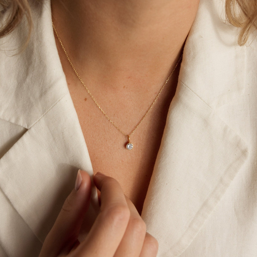 Someone wearing a cream blazer and the Custom Birthstone Necklace, featuring a small, round gold pendant—an elegant and meaningful jewelry piece.