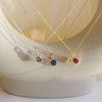 The Zodiac Birthstone Necklace features colored gemstones on silver, gold, and rose gold chains, elegantly displayed on a white curved surface—an ideal personalized jewelry or birthstone necklace gift.
