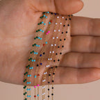 A hand holds delicate gold Beaded Station Necklaces with colorful beads, highlighting trendy styles perfect for playful jewelry lovers.