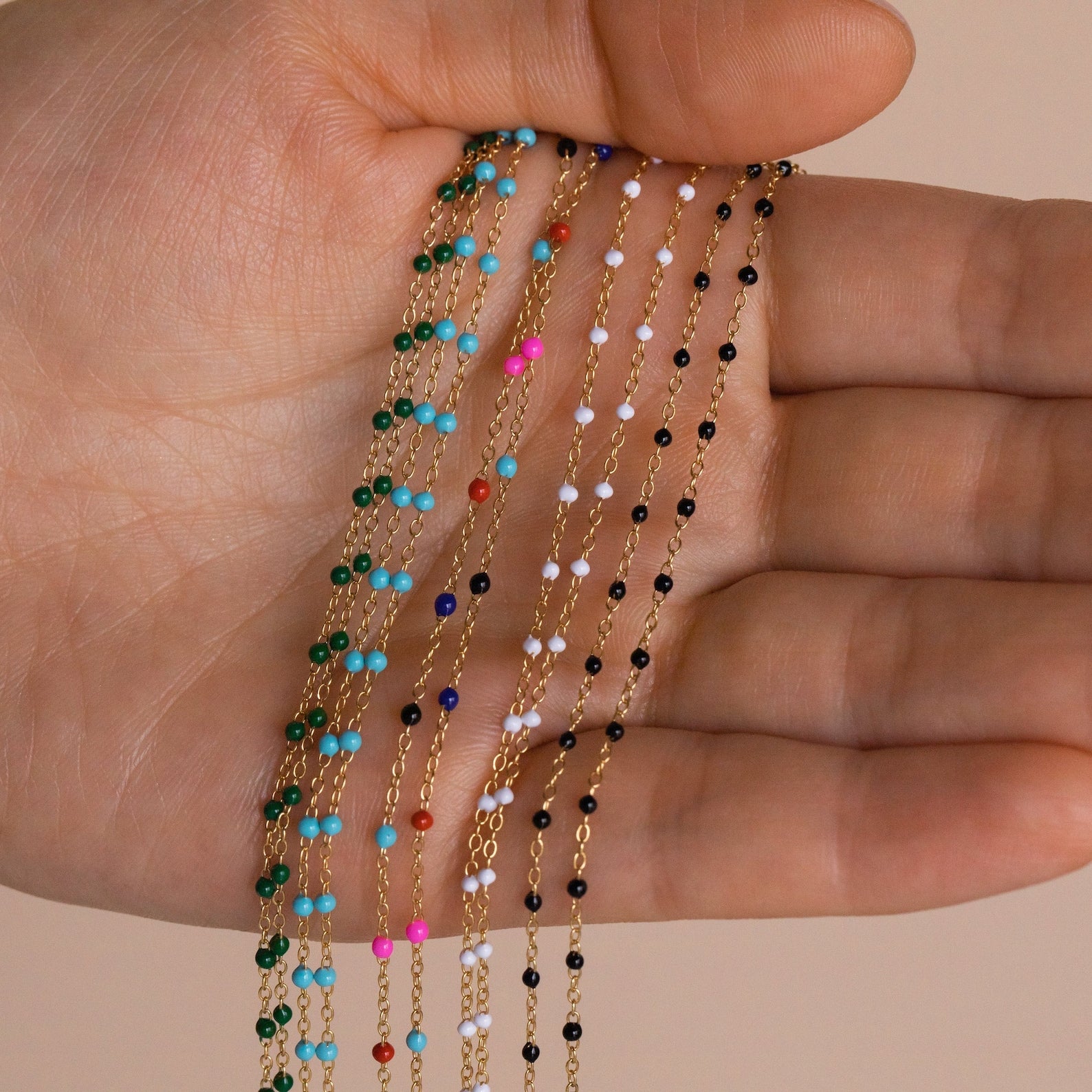 A hand holds delicate gold Beaded Station Necklaces with colorful beads, highlighting trendy styles perfect for playful jewelry lovers.