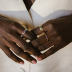 Close-up of hands wearing the Baguette Birthstone Ring alongside vibrant gemstone stacking rings, elegantly paired with a cream-colored coat.