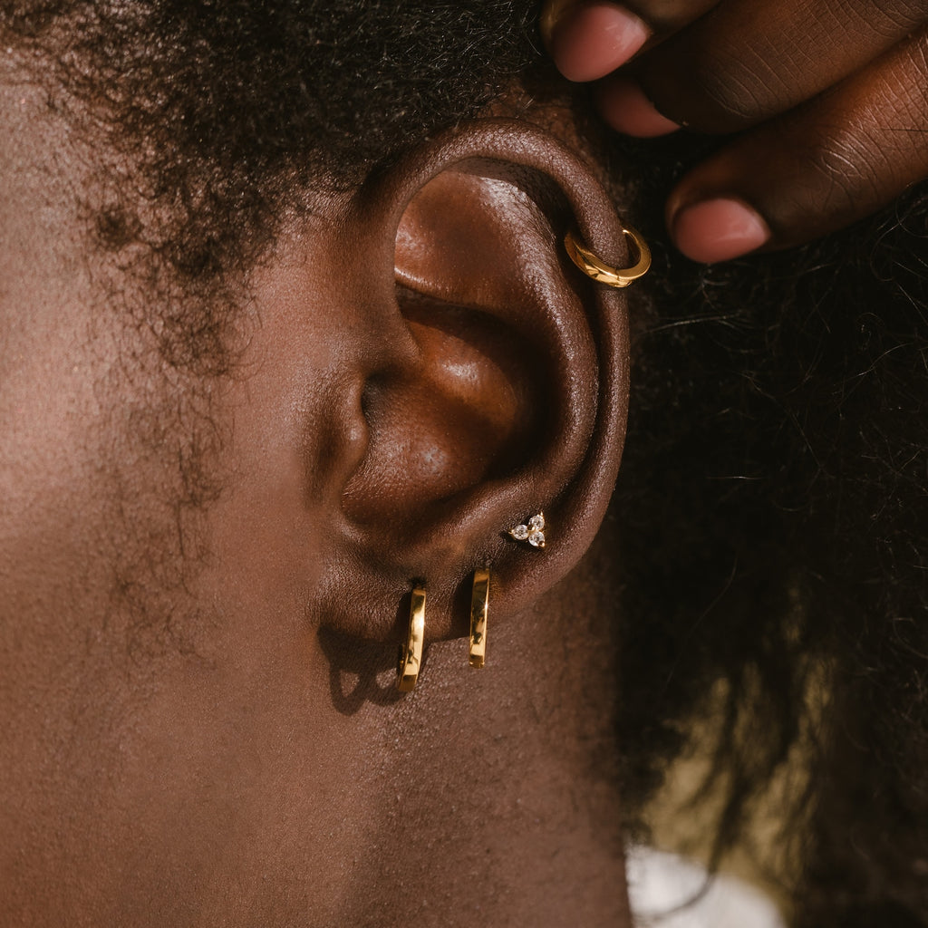 Close-up of an ear wearing the Editor Huggie Earrings Set, featuring dainty hoops, a crystal stud, and a gold upper ear cuff.