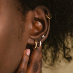 Close-up of a person's ear wearing the Editor Huggie Earrings Set, featuring dainty gold hoop earrings, as a hand gently touches their neck.