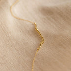 Morse Code Necklace—delicate gold beads and bars on a soft beige fabric backdrop. A perfect personalized gift.