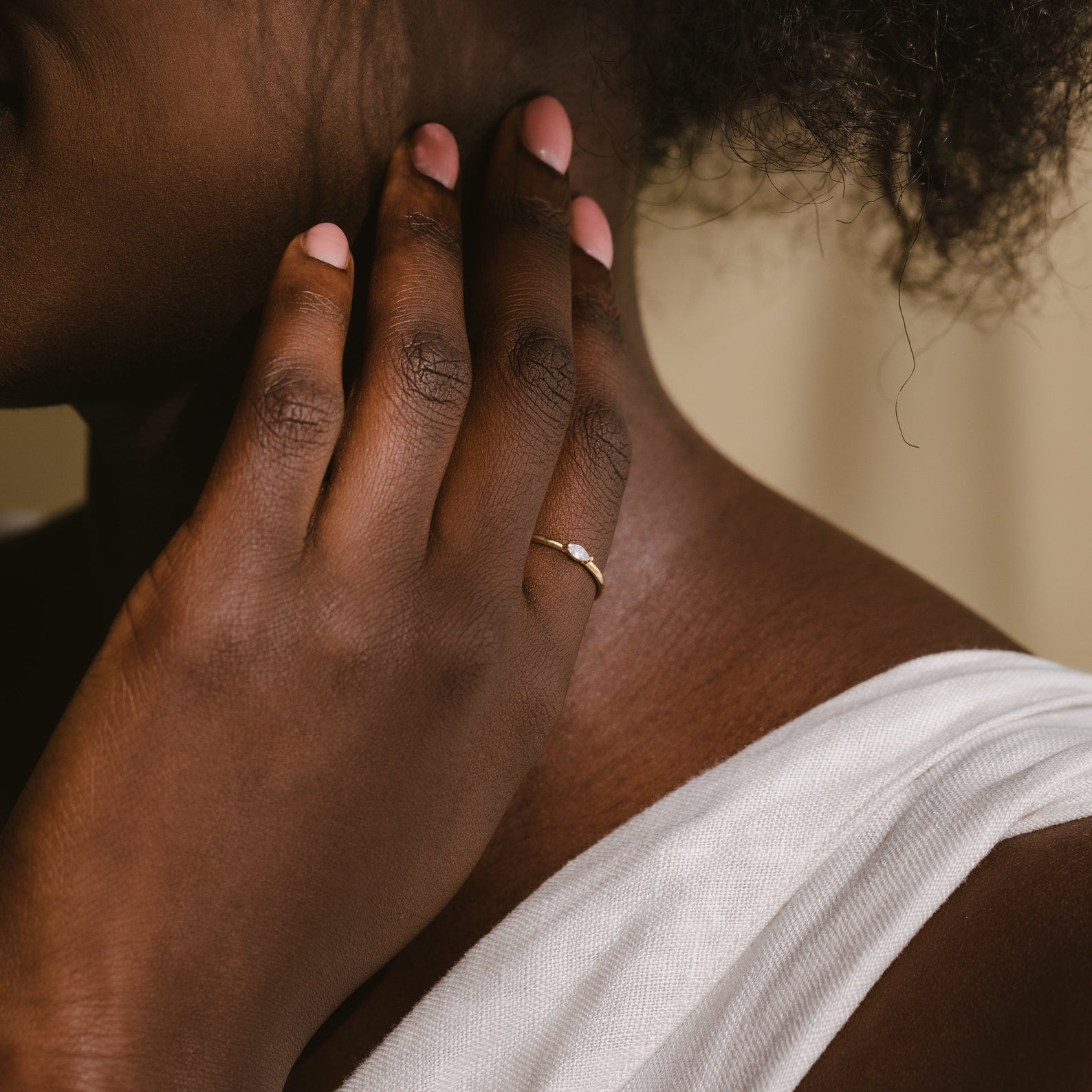 A person touches their neck, displaying the Marquise Birthstone Ring and light pink nail polish, while wearing a white top.