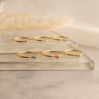 Six Marquise Birthstone Rings with colorful gemstones are showcased on two clear glass platforms against a soft background.
