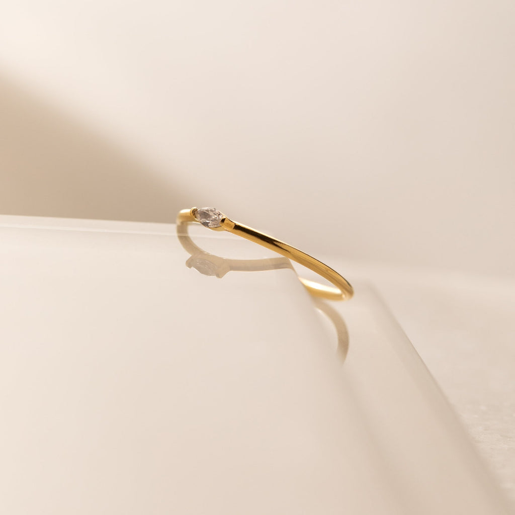 The Marquise Birthstone Ring, featuring a delicate design and a small diamond, rests on a glossy surface with a soft shadow, showcasing its elegant charm.