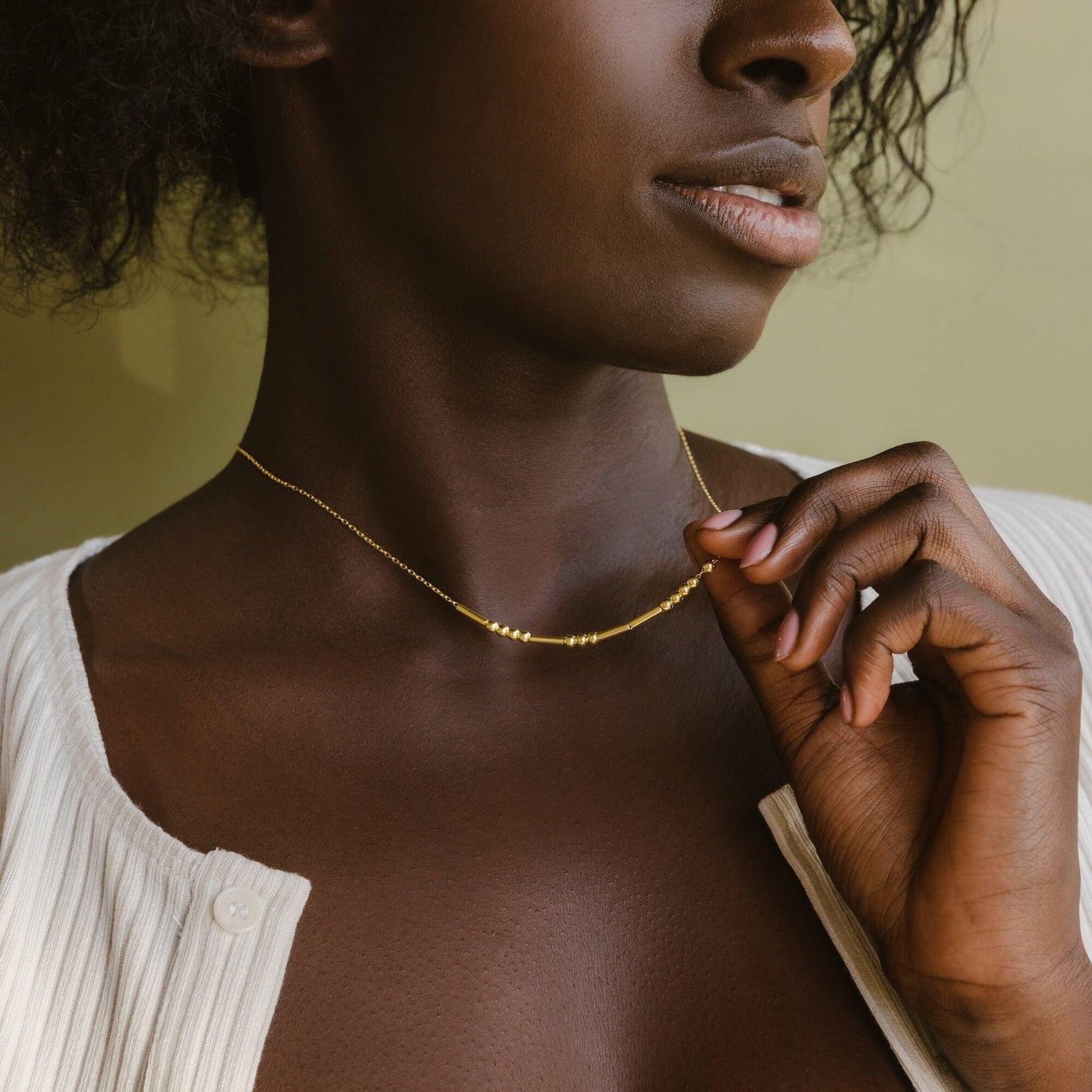 A woman in a white top holds the Morse Code Necklace against her neck, shown from the shoulders up.