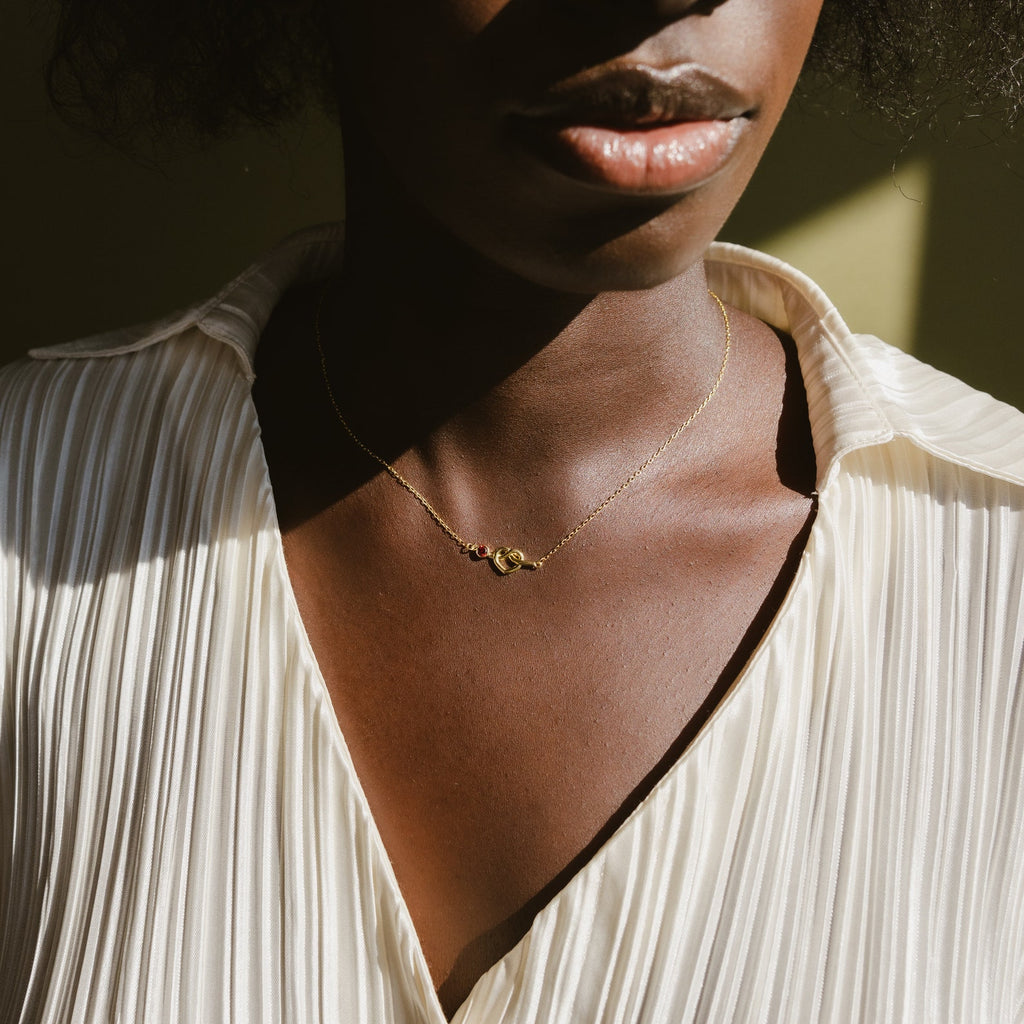 A woman wearing a pleated cream blouse and the Love Knot Birthstone Necklace, sunlight casting gentle shadows on her.
