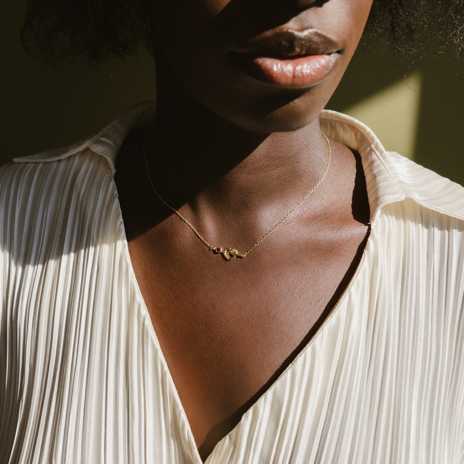 A woman wearing a pleated cream blouse and the Love Knot Birthstone Necklace, sunlight casting gentle shadows on her.