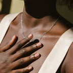 A woman with painted nails touches her chest, wearing a cream top and the Flower Station Necklace—an elegant floral silver piece and the perfect gift for her.