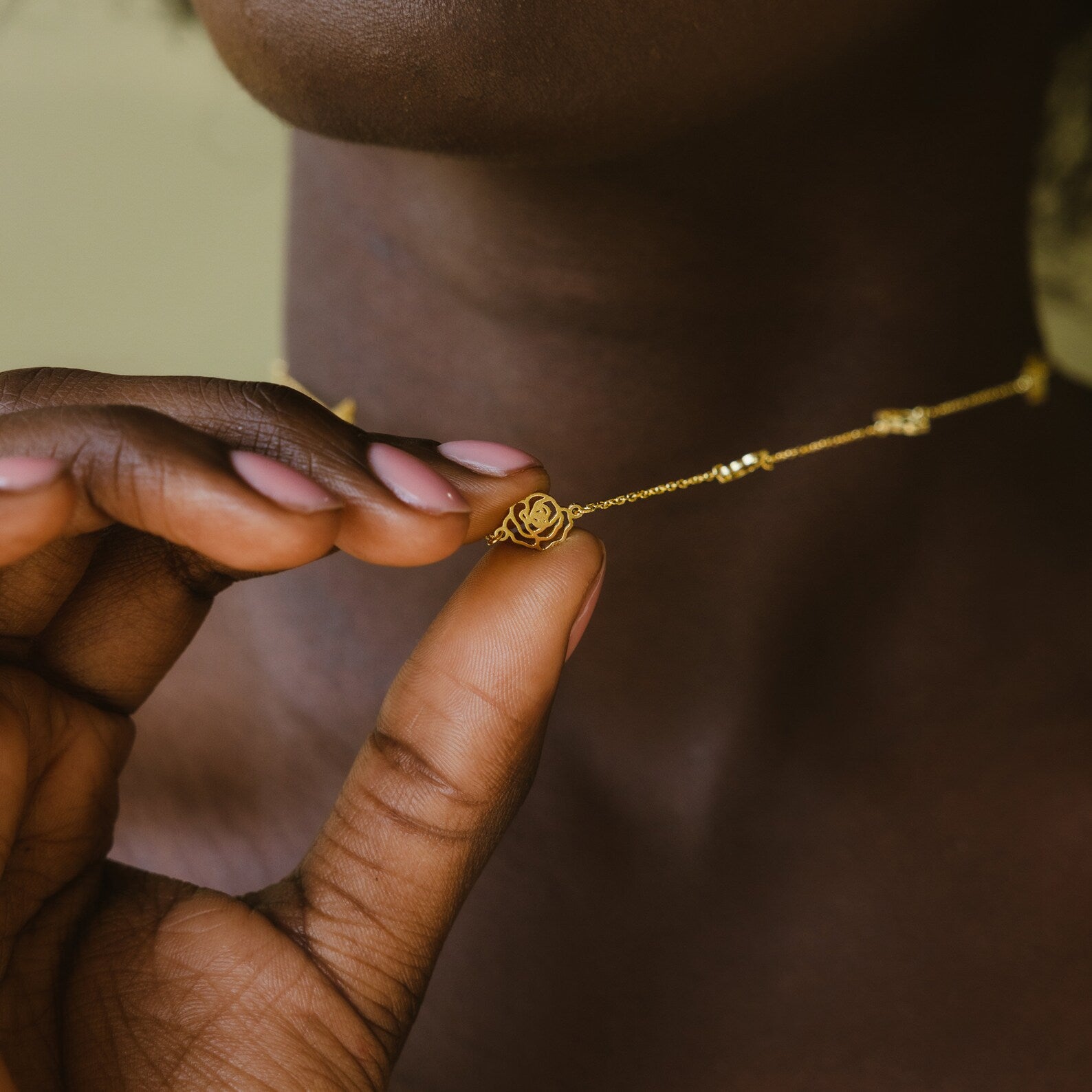 A person holds the Flower Station Necklace, featuring a delicate gold chain and small rose pendant—an elegant floral accessory and perfect gift for her.