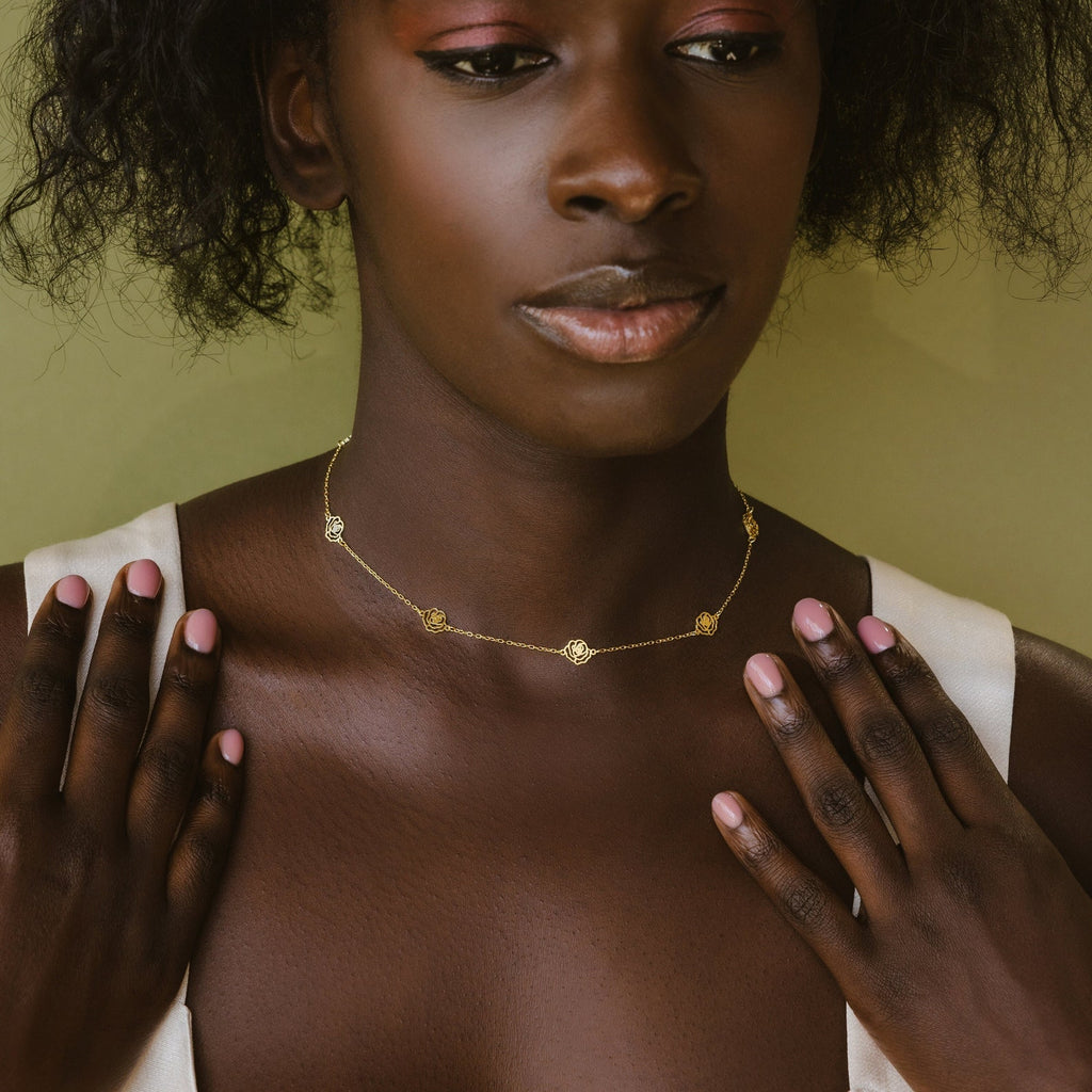 A woman in a white top gently touches her collarbone while wearing the Flower Station Necklace—a delicate floral jewelry gift for her.
