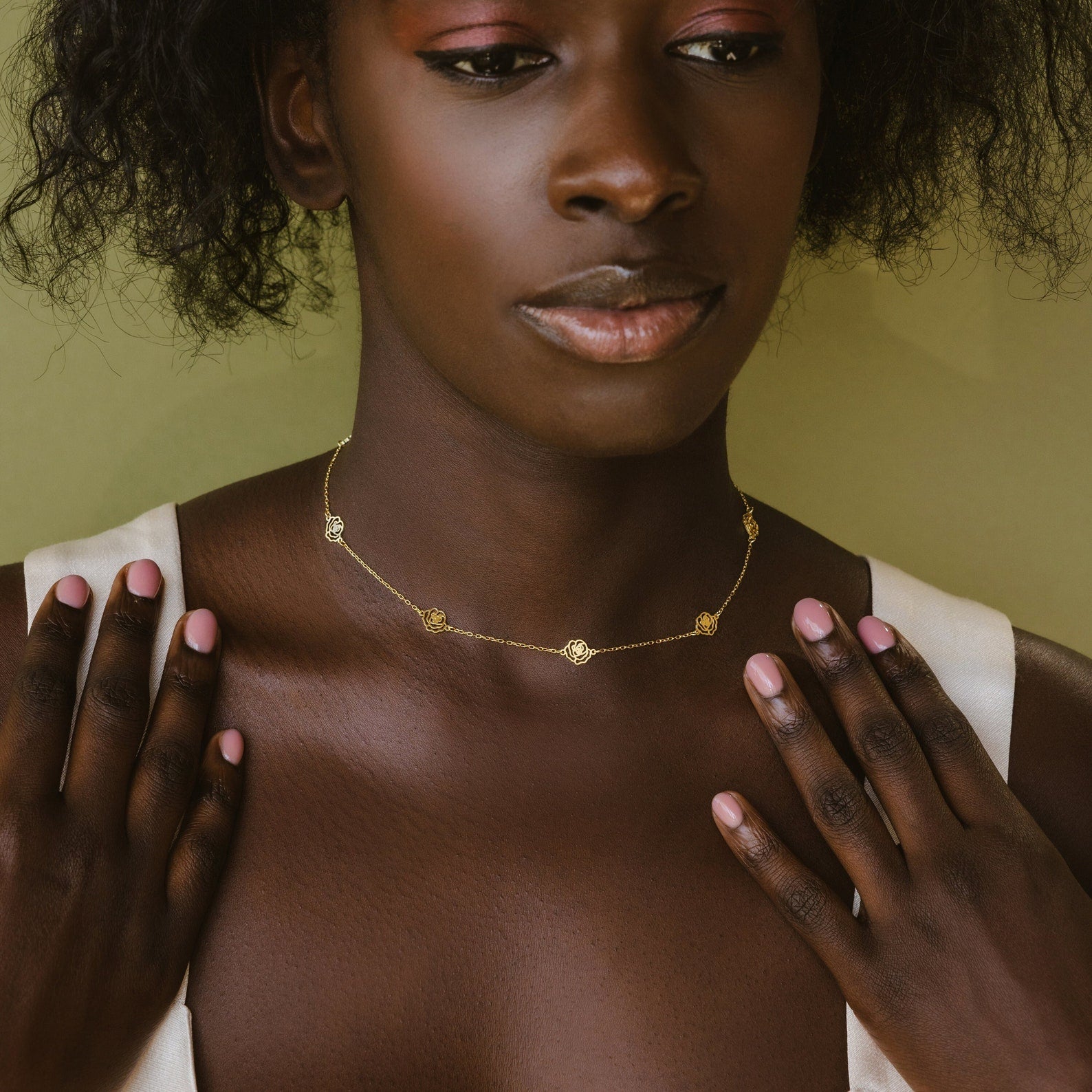 A woman in a white top gently touches her collarbone while wearing the Flower Station Necklace—a delicate floral jewelry gift for her.