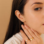 Woman with long brown hair wears gold Starburst Studs and two gold rings as she touches her neck.
