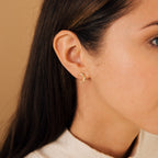 Close-up of a woman’s ear wearing Eclipse Moon Studs, small gold crescent moon earrings adorned with tiny stones—perfect for celestial jewelry lovers.