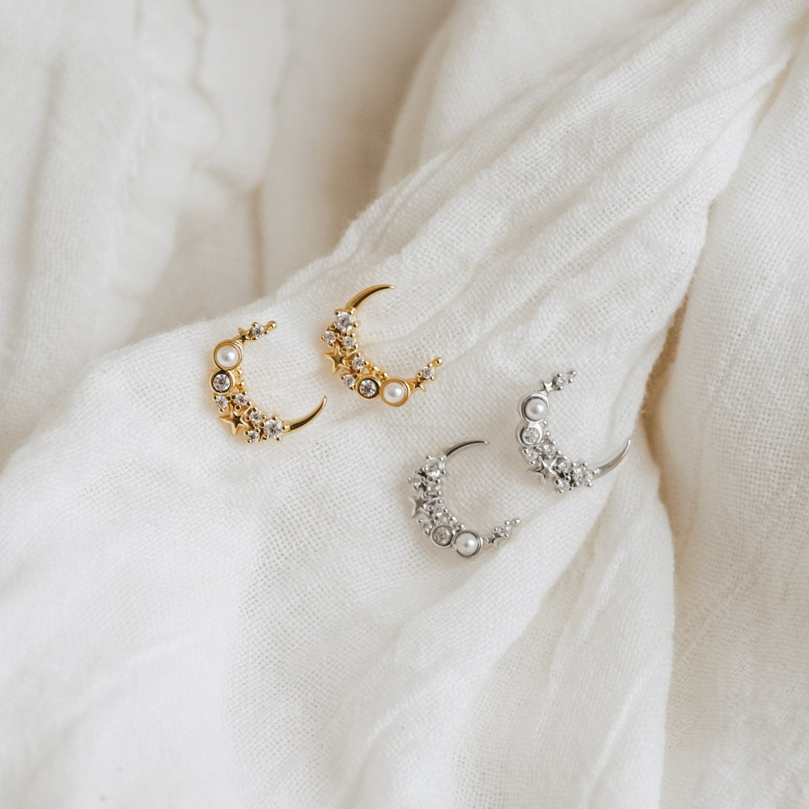 Two pairs of Eclipse Moon Studs, one in gold and one in silver, elegantly displayed on white fabric.