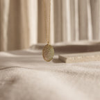 The Oval Fingerprint Necklace showcases a custom fingerprint etching, elegantly displayed on a soft, neutral fabric background—an exquisite memorial jewelry piece to keep memories close.