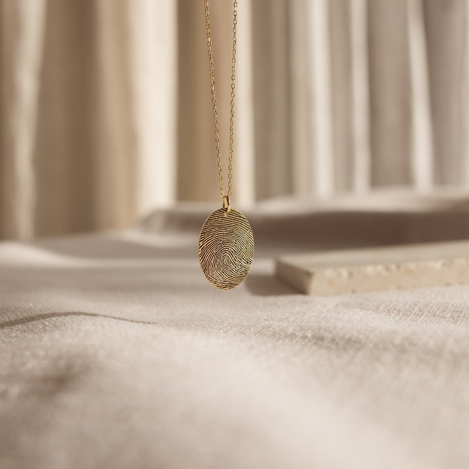 The Oval Fingerprint Necklace showcases a custom fingerprint etching, elegantly displayed on a soft, neutral fabric background—an exquisite memorial jewelry piece to keep memories close.