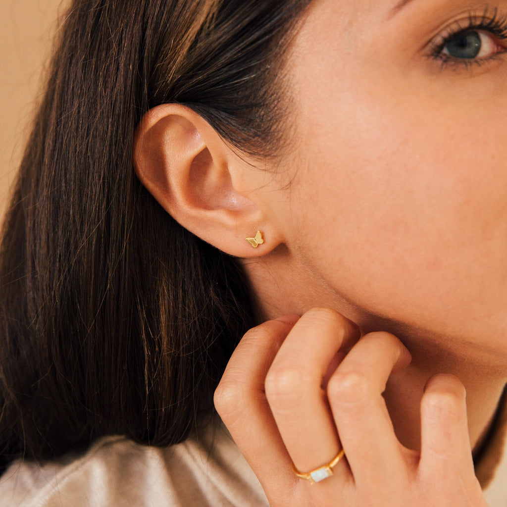 Close-up of a woman’s ear wearing Emilia Butterfly Studs, her hand gently touching her face—a chic choice for those who love trendy gold earrings.