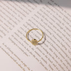 The Fingerprint Oval Ring, a handcrafted gold piece featuring a unique fingerprint design, is displayed on the open pages of a book under gentle lighting.