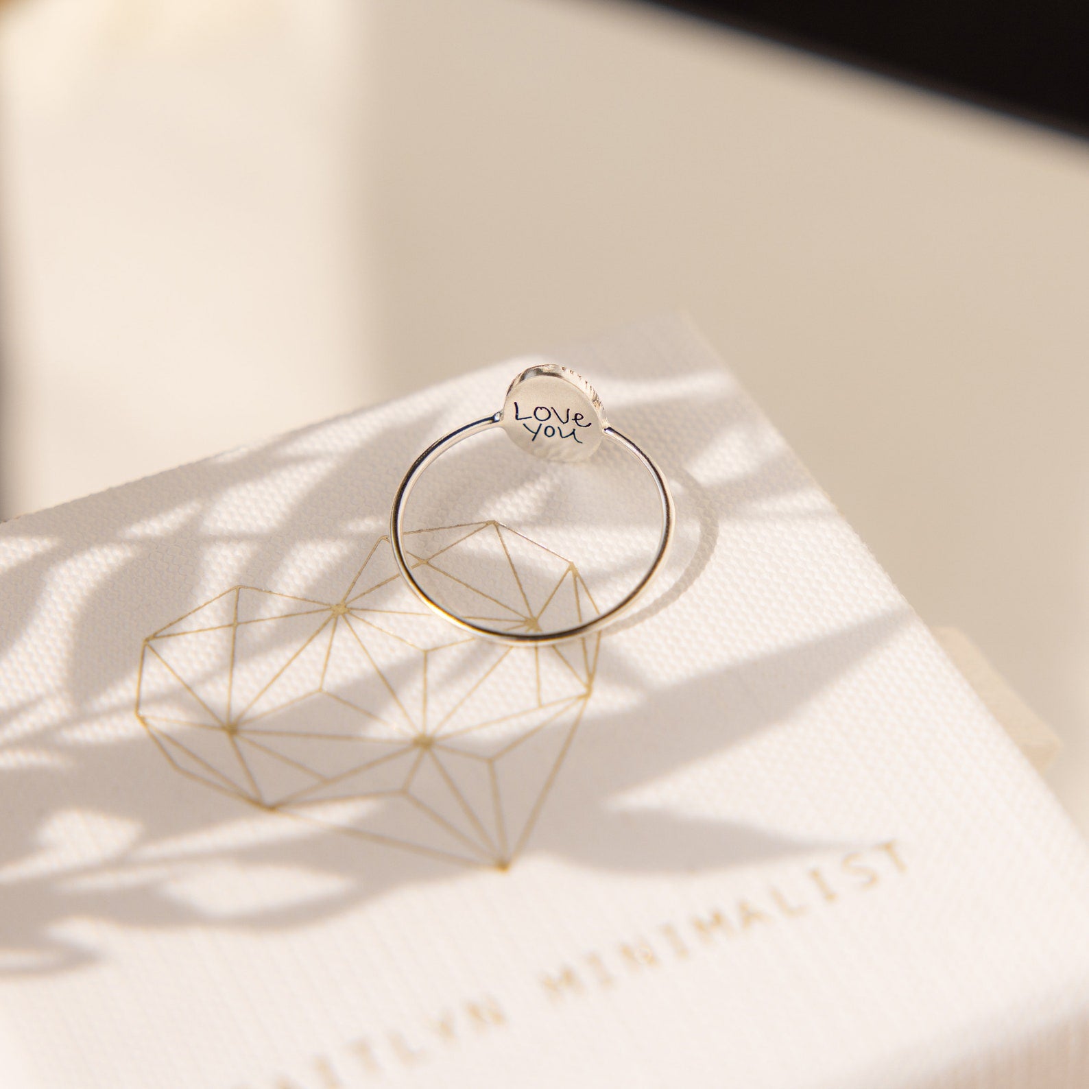 A handcrafted Fingerprint Oval Ring rests on a white box featuring a geometric heart and gold lettering.