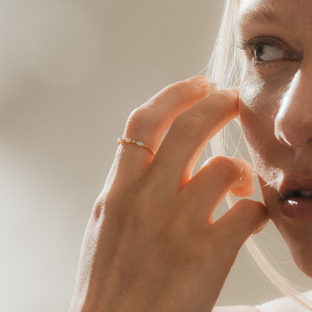 Woman wearing the Alessia Trio Opal Ring on her finger, hand near her face, showcasing the delicate opals catching the light.