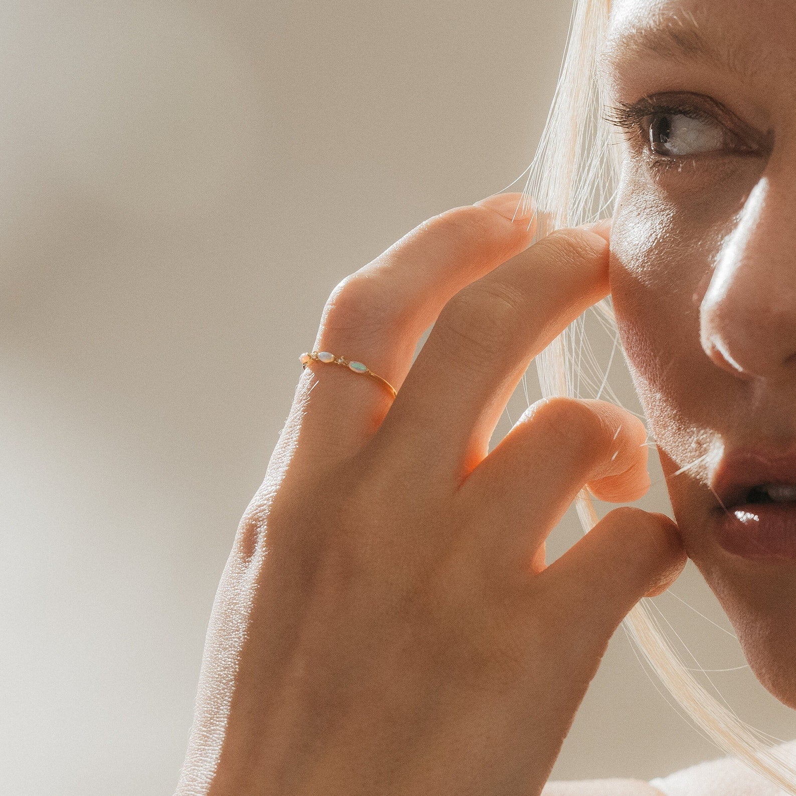 Woman wearing the Alessia Trio Opal Ring on her finger, hand near her face, showcasing the delicate opals catching the light.