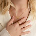 A woman wears a gold Pet Initial Necklace and a matching ring with the number "18," paired with a light blouse—an unforgettable gift idea for pet lovers.
