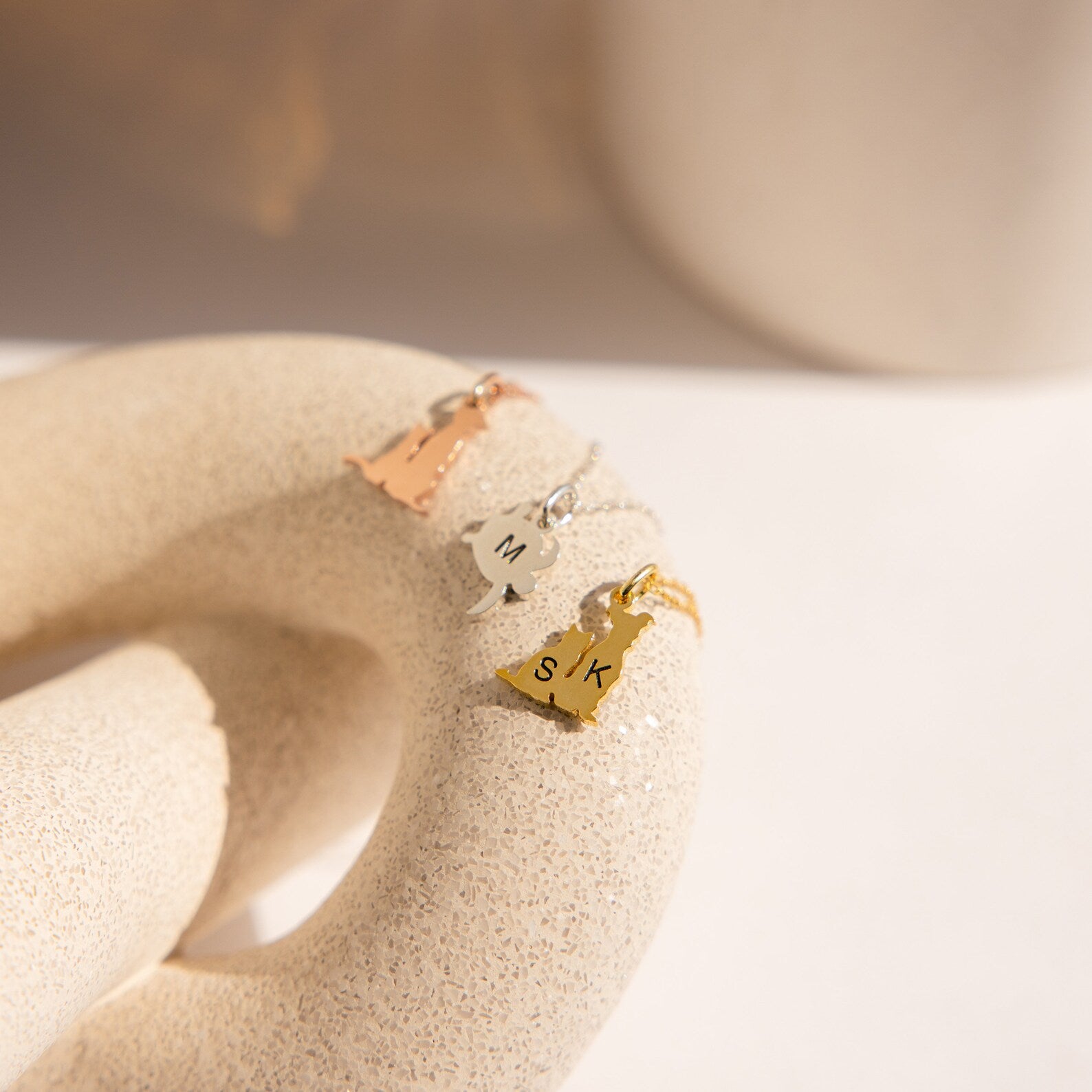 The Pet Initial Necklace features three state-shaped metallic pendants on chains, each engraved with initials and displayed on a textured ring—an ideal personalized necklace and thoughtful gift for pet lovers.