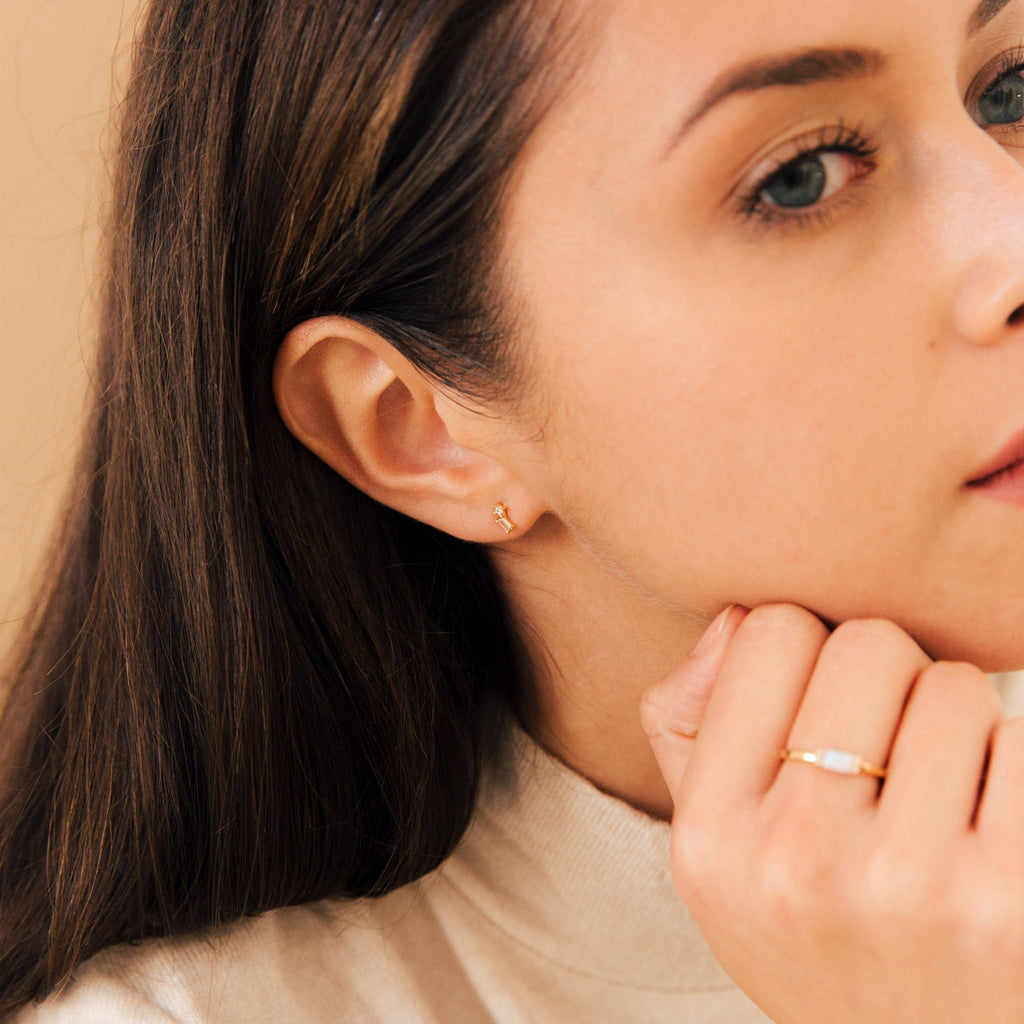 Woman with long brown hair wears the Blair Baguette Diamond Drop Studs and a gold ring with a white stone, creating an effortlessly minimalist look.