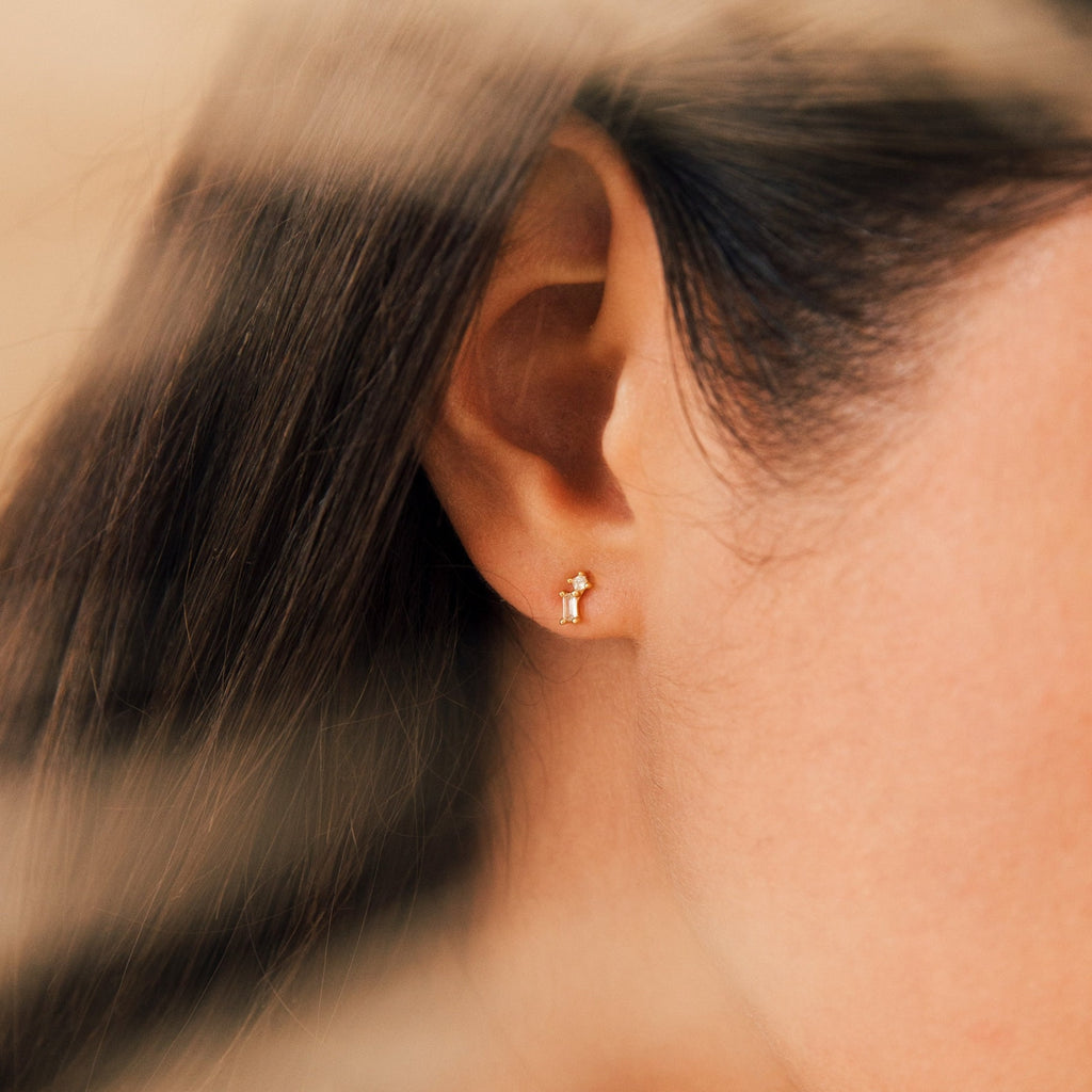 Close-up of a woman's ear wearing the Blair Baguette Diamond Drop Studs—minimalist gold earrings featuring a sleek design with sparkling diamond accents.