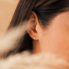 Close-up of a woman's ear with straight brown hair, wearing Blair Baguette Diamond Drop Studs—dainty gold earrings ideal for those who love minimalist jewelry.