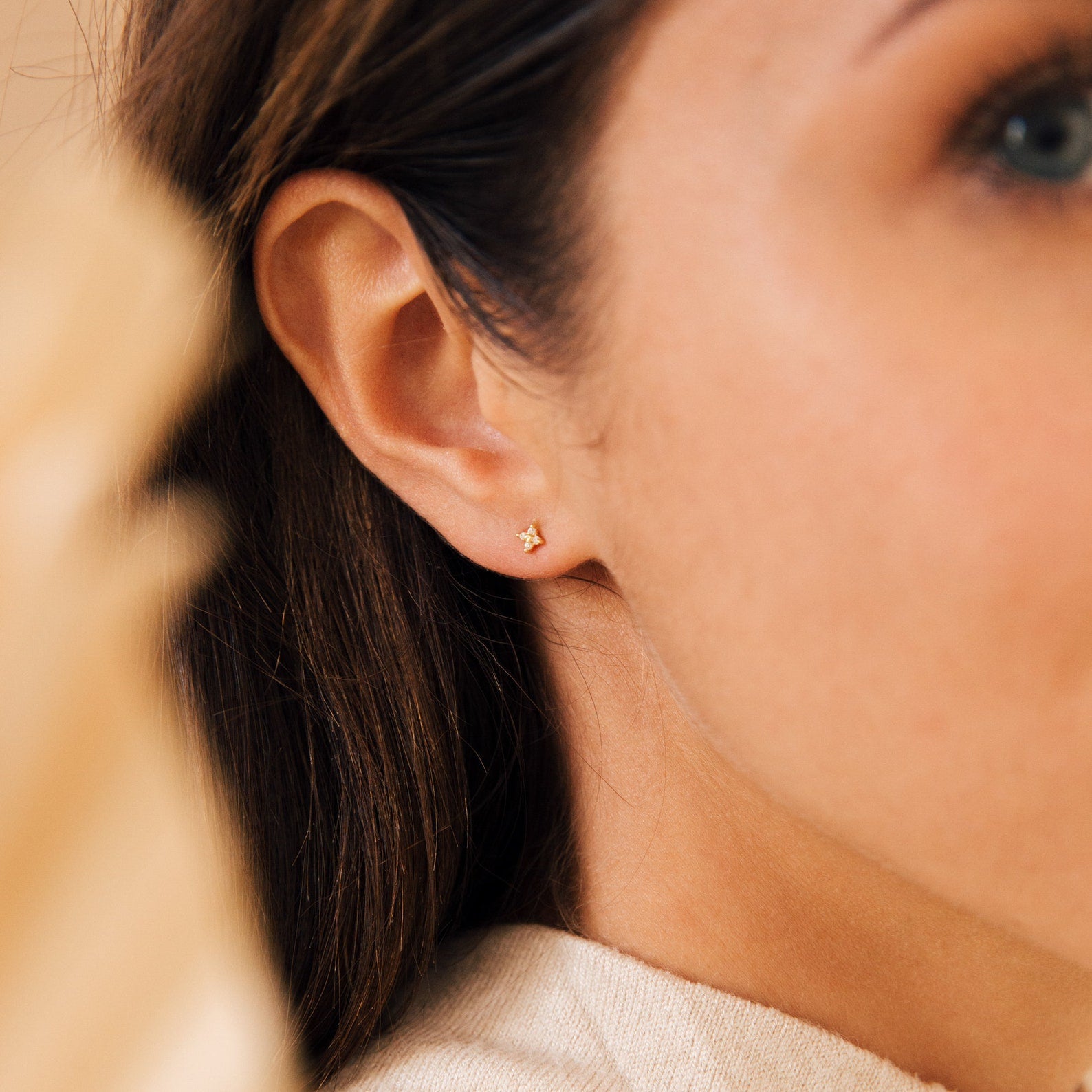 Close-up of a woman wearing our Hera Flower Stud earring with a subtle sparkle, with her dark brown hair tucked behind her ear.