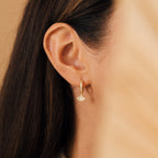 Close-up of a woman's ear wearing Aleah Opal Evil Eye Huggies, gold hoop earrings featuring an opal evil eye design, with long brown hair.