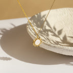 Gold necklace with a sun-shaped pendant featuring a smooth mothr of pearl with round shape in center, displayed against a textured ceramic bowl in warm natural light.