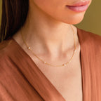 A woman in a rust-colored blouse wears the Dainty Pearl Station Necklace with small pearls—a timeless piece that's a perfect gift for mom.