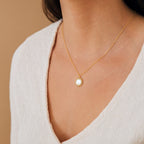 Wearing the Elia Sun Necklace, featuring a gold sun-shaped pendant with a white stone, paired with a cream V-neck top, she radiates effortless boho-luxe style.