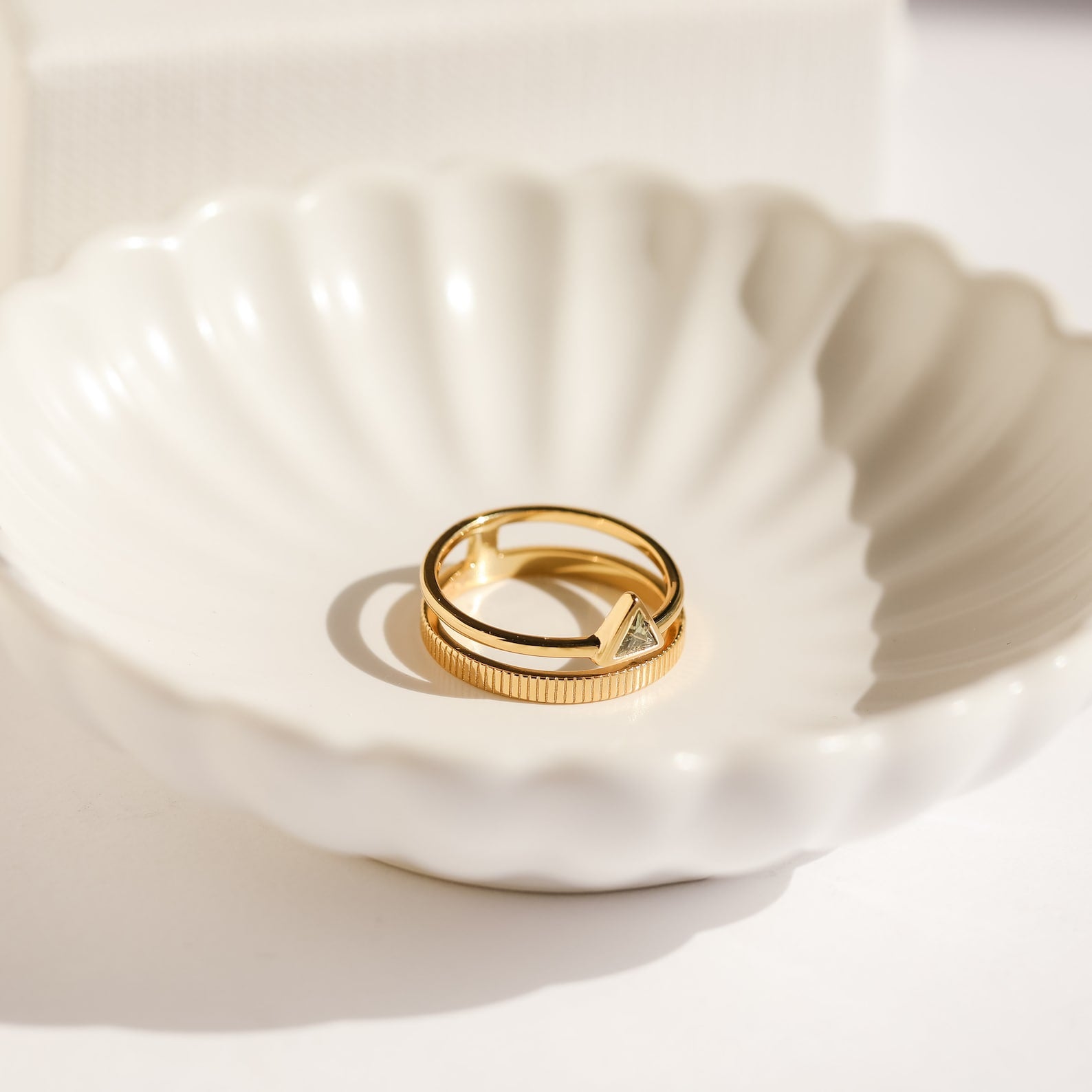The Jaida Peridot Duo Ring rests in a white scalloped ceramic dish on a light surface.