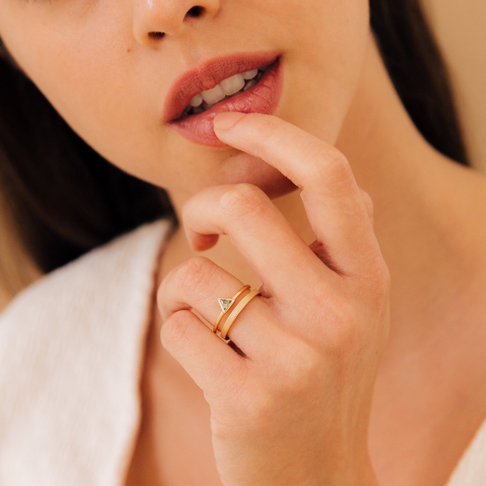 A woman touches her lips with her finger, wearing the elegant Jaida Peridot Duo Ring featuring a gold Art Deco design and two peridot gems.