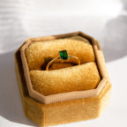 Harley Emerald Ring—an art deco gold ring with a rectangular green gemstone, presented in a yellow velvet hexagonal box and sunlit on a white surface. Ideal for vintage jewelry lovers.