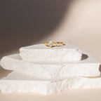 The Harlow Diamond Ring in 18K Gold, featuring a marquise diamond, is displayed on stacked white stone slabs.