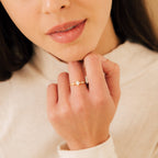 A woman gently touches her chin, displaying the Harlow Diamond Ring in 18K Gold on her finger.