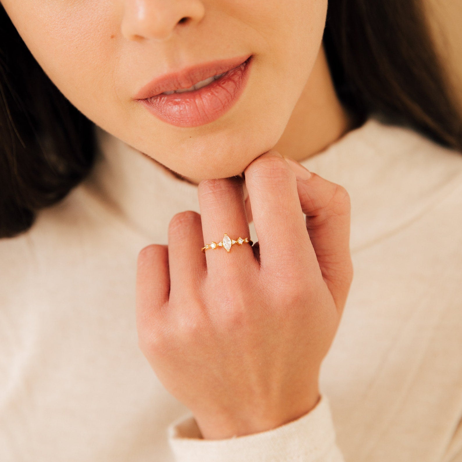 A woman gently touches her chin, displaying the Harlow Diamond Ring in 18K Gold on her finger.