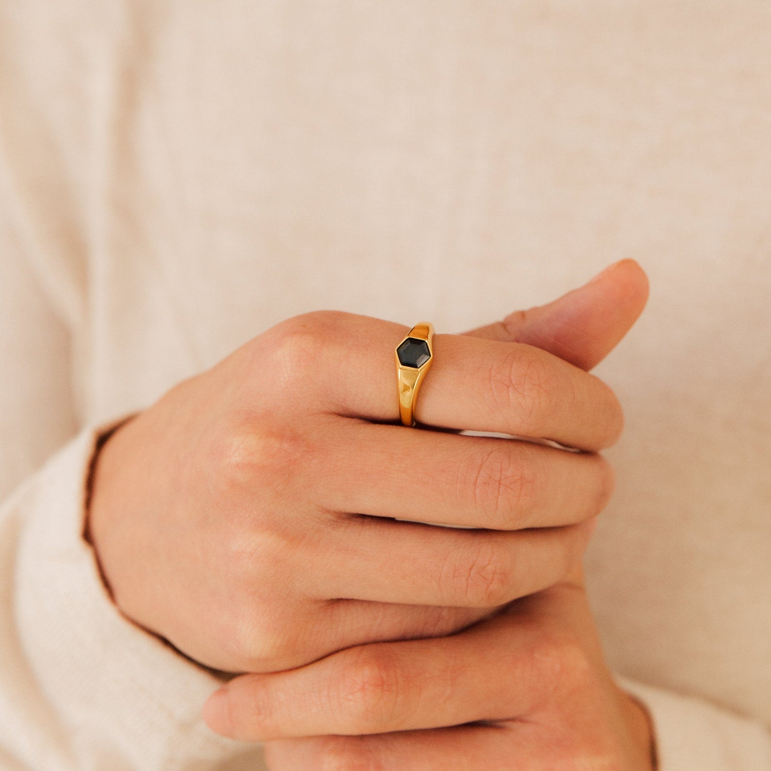 Close-up of a hand wearing the Ember Signet Ring, a gold chunky ring featuring a small black hexagonal stone on the middle finger—an ideal stylish men’s gift.