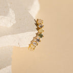 Gold earring with various gemstones displayed on a textured off-white stone background, paired beautifully with the Mosaic Wave Eternity Ring.